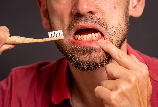 closeup of a man brushing his teeth exposing his bleeding gums