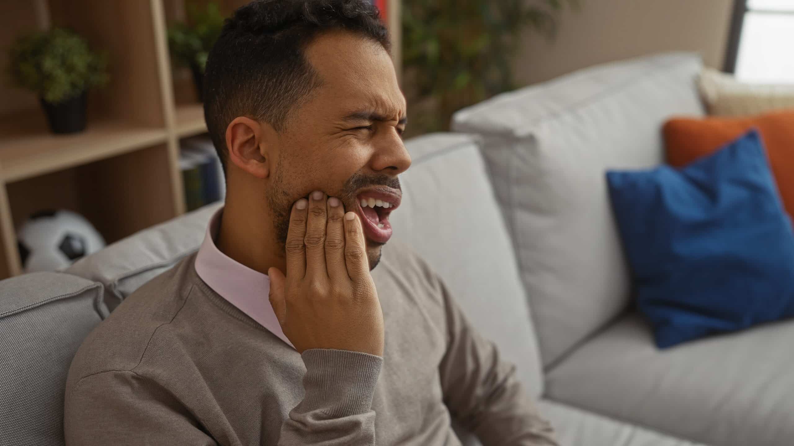 young man sitting on a couch with severe tooth pain, holding jaw
