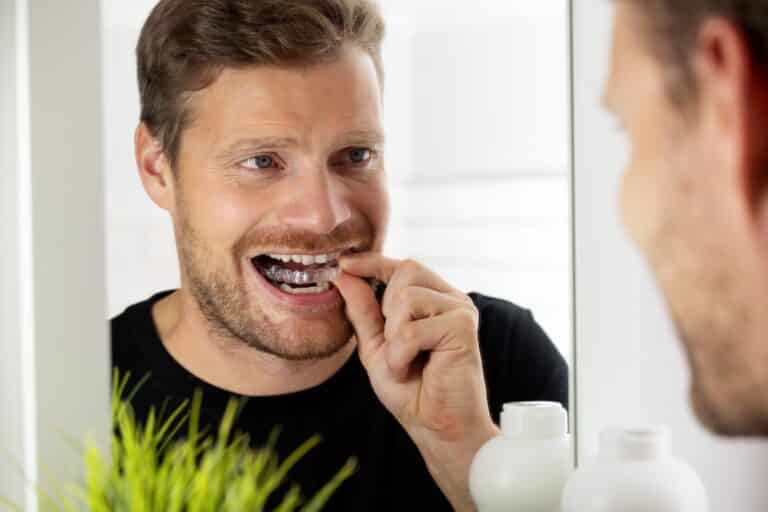 adult man inserting his clear aligners while looking in mirror